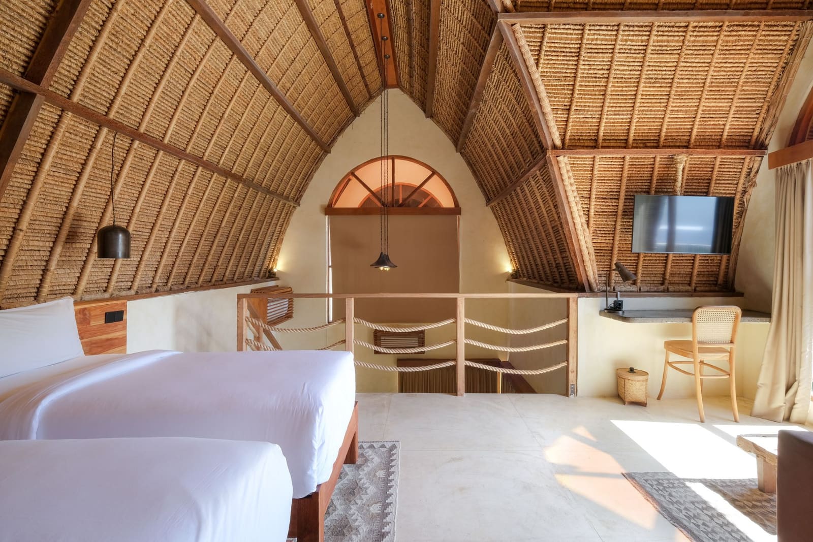 A room at Lulu's: a vaulted alang-alang roof over two beds and a desk by the window.